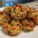 A pile of perfectly cooked, golden brown air fryer shrimp coated in garlic and herbs on a white plate.