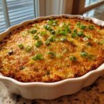 A baked, cheesy popper dip in a white ruffled dish, topped with fresh green onions.