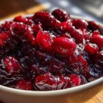 Close-up of glistening, homemade cranberry sauce with whole berries in a small white bowl.