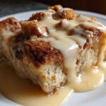 Close-up of a rich slice of bread pudding topped generously with creamy vanilla sauce.