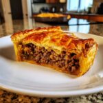 A close-up slice of amazing meat pie featuring a thick, savory ground meat filling and golden, flaky puff pastry crust.