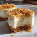 Close-up of two mini cheesecake bites, one with a bite taken out, showing creamy filling and crumb topping.