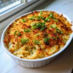 Close-up of a baked popper dip in a white oval dish, featuring a golden, crispy topping and fresh green onions.