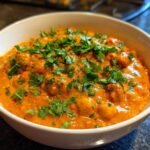A close-up of a vibrant orange pumpkin curry with chickpeas, topped generously with fresh chopped cilantro.