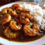 Close-up of a plate featuring rich shrimp etouffee with plump shrimp in a dark roux sauce, served alongside fluffy white rice.