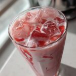 Close-up overhead view of a tall glass filled with homemade strawberry milk and large ice cubes.