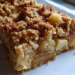 A close-up shot of a square serving of apple baked oatmeal featuring a thick, moist base and a crunchy, cinnamon-sugar crumble topping.