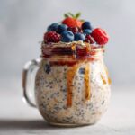 Close-up of berry overnight oats in a glass jar, topped with fresh fruit and drizzled with honey.