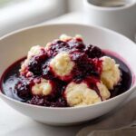 Close-up of fluffy, cooked Blackberry Dumplings served warm in a bowl, generously topped with a dark, rich blackberry sauce.