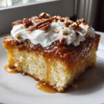 A moist slice of butter pecan praline poke cake topped with caramel sauce, whipped cream, and chopped pecans.