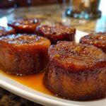 Five glistening, round portions of candied sweet potatoes covered in a rich, dark glaze, served on a white plate.