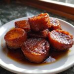 Close-up of thick slices of candied sweet potatoes glistening with rich, dark syrup on a white plate.