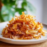A close-up shot of a mound of deeply golden brown caramelized onions served on a light plate.