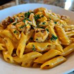 A close-up shot of creamy, cheesy chicken pasta made with penne, topped with parsley.