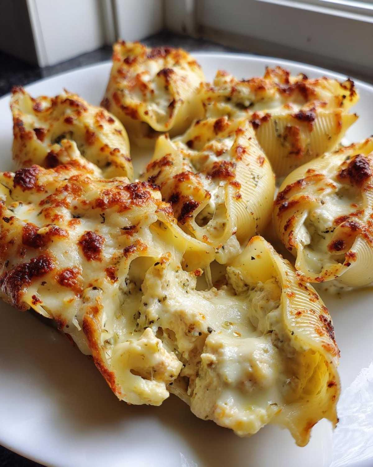 Close-up of baked chicken alfredo stuffed shells with melted, browned cheese topping.