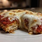 Close-up of a baked chicken parmesan recipe cut open, showing breaded chicken, marinara sauce, and melted, bubbly mozzarella cheese.