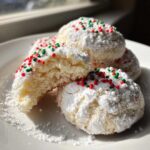 Close-up of soft Christmas gooey butter cookies coated in powdered sugar and red/green sprinkles.