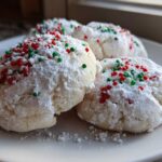 Close-up of three Christmas gooey butter cookies heavily dusted with powdered sugar and festive red and green sprinkles.