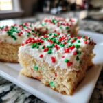 Three squares of moist christmas sugar cookie bars topped with white frosting and red and green holiday sprinkles.