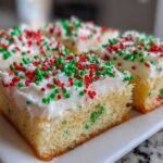 Four squares of moist christmas sugar cookie bars topped with thick white frosting and red and green holiday sprinkles.