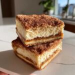 Two stacked squares of rich churro cheesecake bars topped generously with cinnamon sugar.