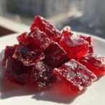 Close-up of deep red, sugar-coated cinnamon rock candy cubes piled on a white plate.