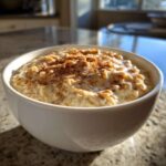 Close-up of a white bowl filled with creamy banana oatmeal, topped generously with cinnamon.