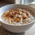 Close-up of creamy banana oatmeal in a white bowl, drizzled with honey and sprinkled with cinnamon.