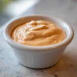 Close-up of creamy, orange-hued big mac sauce texture in a small white dipping bowl.