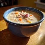 Close-up of creamy ham bean soup topped with shredded ham and carrots in a rustic blue bowl.