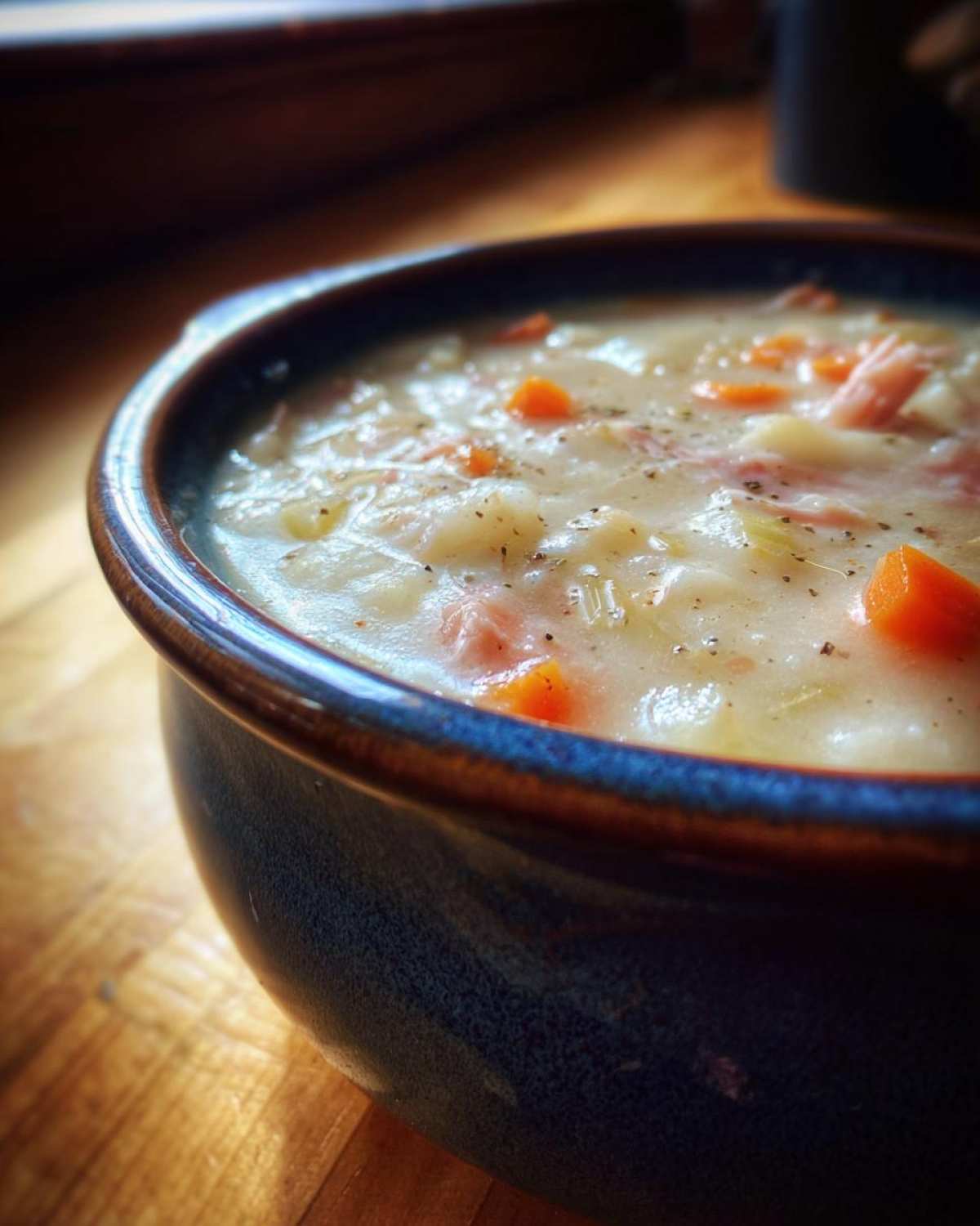 Close-up of a creamy, hearty bowl of ham bean soup with visible chunks of carrots and seasoning.