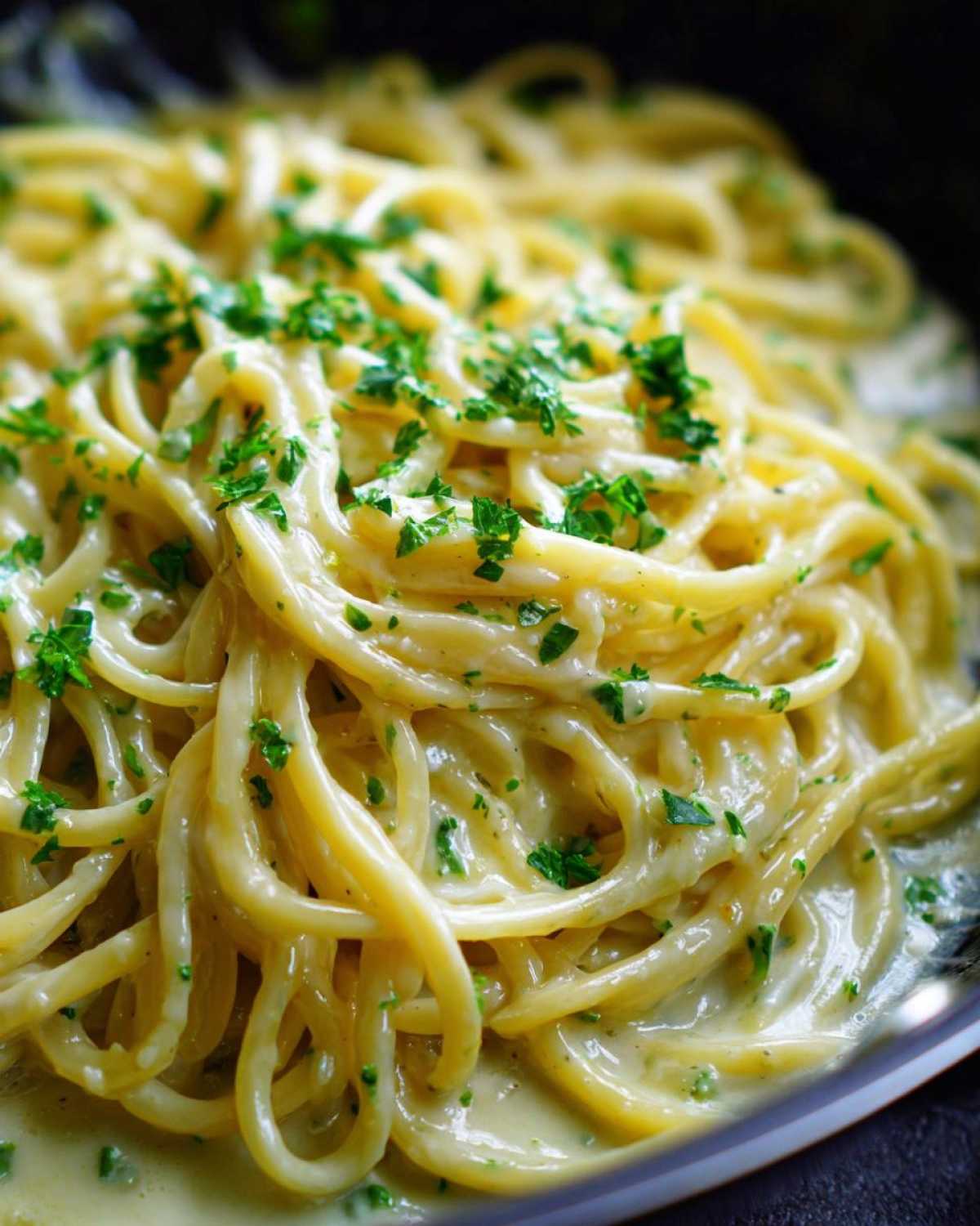 A close-up shot of spaghetti coated in a rich, creamy lemon sauce, garnished with fresh chopped parsley.