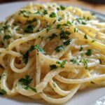 A close-up shot of perfectly twirled creamy lemon pasta tossed in a light sauce and topped with fresh green parsley.