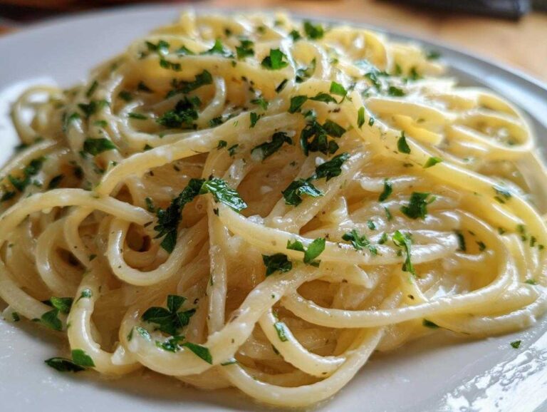 A close-up shot of perfectly twirled creamy lemon pasta tossed in a light sauce and topped with fresh green parsley.