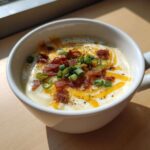 Close-up of creamy loaded baked potato soup topped with melted cheese, crispy bacon bits, and fresh green onions.