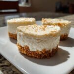 Three creamy, individual mini cheesecake bites with graham cracker crusts sitting on a white plate.