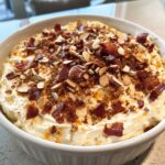 Close-up of creamy Neiman Marcus dip topped generously with crispy bacon pieces and sliced almonds.