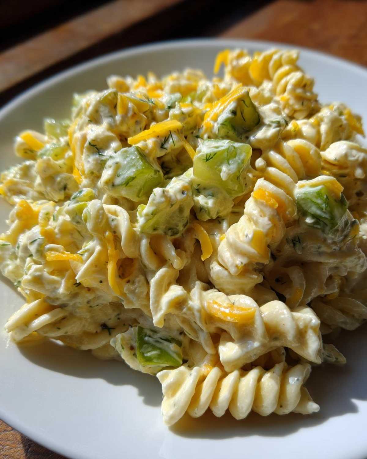 Close-up of creamy pickle pasta salad made with rotini, green pickle chunks, and shredded cheddar cheese.