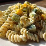 Close-up of creamy pickle pasta salad featuring fusilli pasta, diced pickles, and yellow bell pepper pieces.