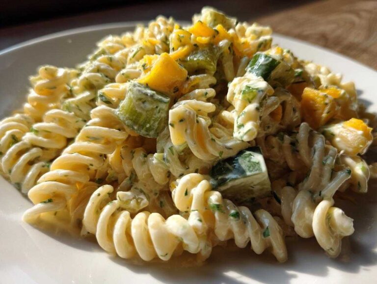 Close-up of creamy pickle pasta salad featuring fusilli pasta, diced pickles, and yellow bell pepper pieces.