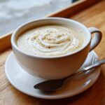 A close-up of creamy roasted cauliflower soup topped with a swirl of cream and spices in a white mug.