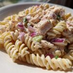 Close-up of creamy tuna pasta salad made with fusilli pasta, chunks of tuna, and diced red onion.