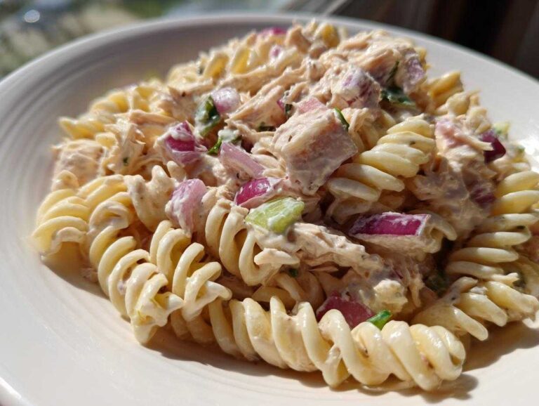 Close-up of creamy tuna pasta salad made with fusilli pasta, chunks of tuna, and diced red onion.