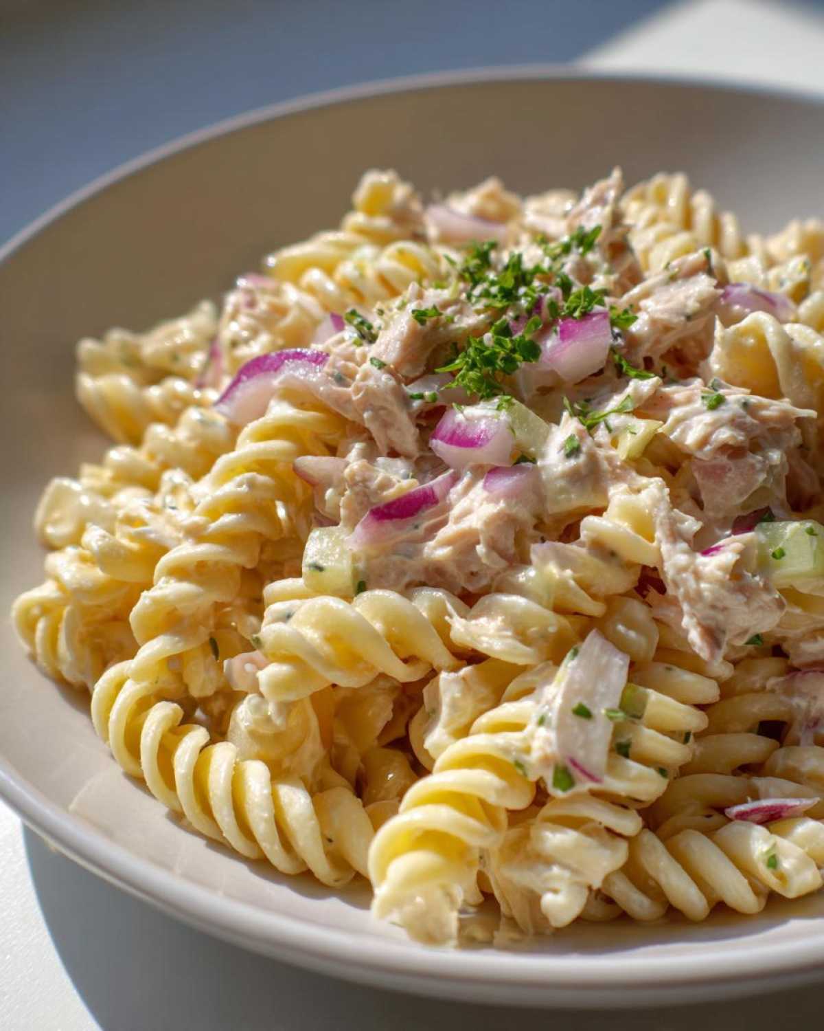 Close-up of creamy tuna pasta salad made with rotini pasta, red onion, and topped with fresh parsley.