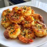 Close-up of crispy, golden brown air fryer shrimp piled high on a white plate, sprinkled with green herbs.