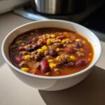 Close-up of a white bowl filled with rich crockpot cowboy soup featuring ground beef, kidney beans, and corn.