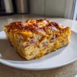 A close-up of a square slice of Croissant Breakfast Casserole featuring layers of flaky pastry, ham, and melted cheese.