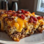 A close-up, featured image of a hearty slice of bacon cheeseburger casserole topped with melted cheddar and crispy bacon pieces.