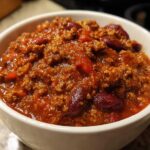 Close-up of a white bowl filled with rich, thick high protein chili featuring ground meat and dark red kidney beans.