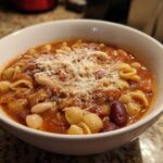 A close-up of a white bowl filled with hot pasta e fagioli soup, topped with grated Parmesan cheese.